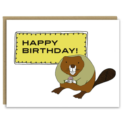 A greeting card with a hand-drawn illustration of a rotund beaver wearing an olive green sweater and holding a cupcake with a pink swirl of frosting standing in front of a sign that reads, " Happy Birthday!" Shown with a Kraft paper envelope on a white background. 