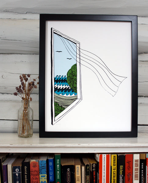 A print of a hand-drawn illustration of a window looking out on ocean waves, a beach and seagulls, a sheer curtain blows in from the window. Shown in a black frame on top of a bookcase in front of a whitewashed log wall. 