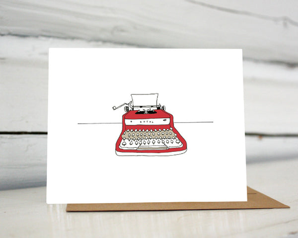 A greeting card showing a hand-drawn illustration of red Royal vintage typewriter with a piece of blank paper loaded in it. Shown standing on a Kraft paper envelope in front of a white-washed log wall. 