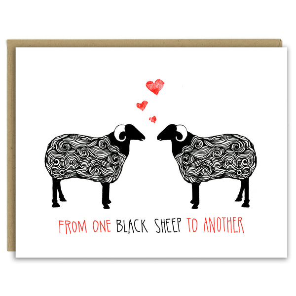 A greeting card with a hand-drawn ink illustration of a pair of black and white sheep with horns facing each other with three hearts over their heads. A hand-lettered message reads, "From one black sheep to another." Shown with a Kraft paper envelope on a white background. 