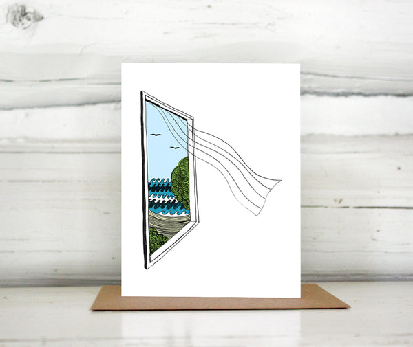 A greeting card showing a hand-drawn illustration of a window looking out on ocean waves, a beach and seagulls, a sheer curtain blows in from the window. Shown standing on a Kraft paper envelope in front of a white-washed log wall. 