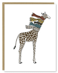 A greeting card showing a hand-drawn illustration of giraffe wearing five knit scarves on its neck. Shown with a Kraft paper envelope on a white background. 