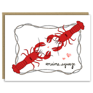 A greeting card with a hand-drawn ink illustration of two bright red lobsters facing each other with hearts around and a frame of nautical roping. The hand-lettered message reads, "Maine Squeeze." Shown with a Kraft paper envelope on a white background. 