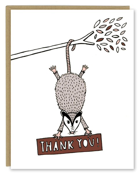 A greeting card showing a hand-drawn illustration of a possum hanging from a tree branch hiding a sign with a hand-lettered message that reads,"Thank you!" Shown with a Kraft paper envelope on a white background. 