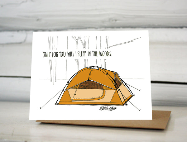 A greeting card showing a hand-drawn illustration of an orange tent in the woods with two pairs of shoes out front. The card has a hand-lettered message reading, "Only for you will I sleep in the woods."  Shown standing on a Kraft paper envelope in front of a white-washed log wall.  