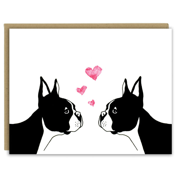 A greeting card with a hand-drawn illustration of two Boston terriers facing each other with three little hearts rising above their heads. Shown with a Kraft paper envelope on a white background. 